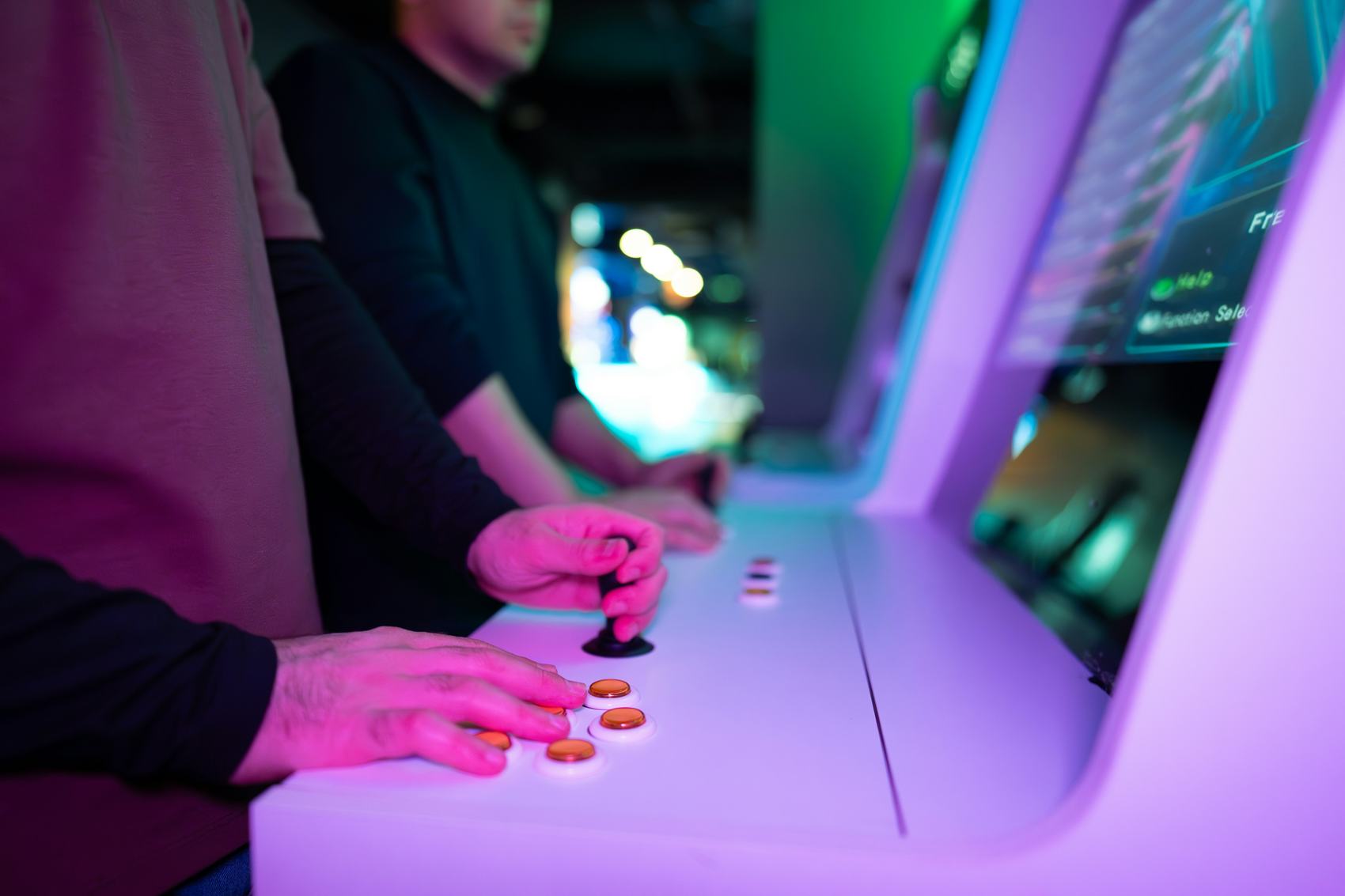 Players at a row of arcade cabinets lit in pink and green
