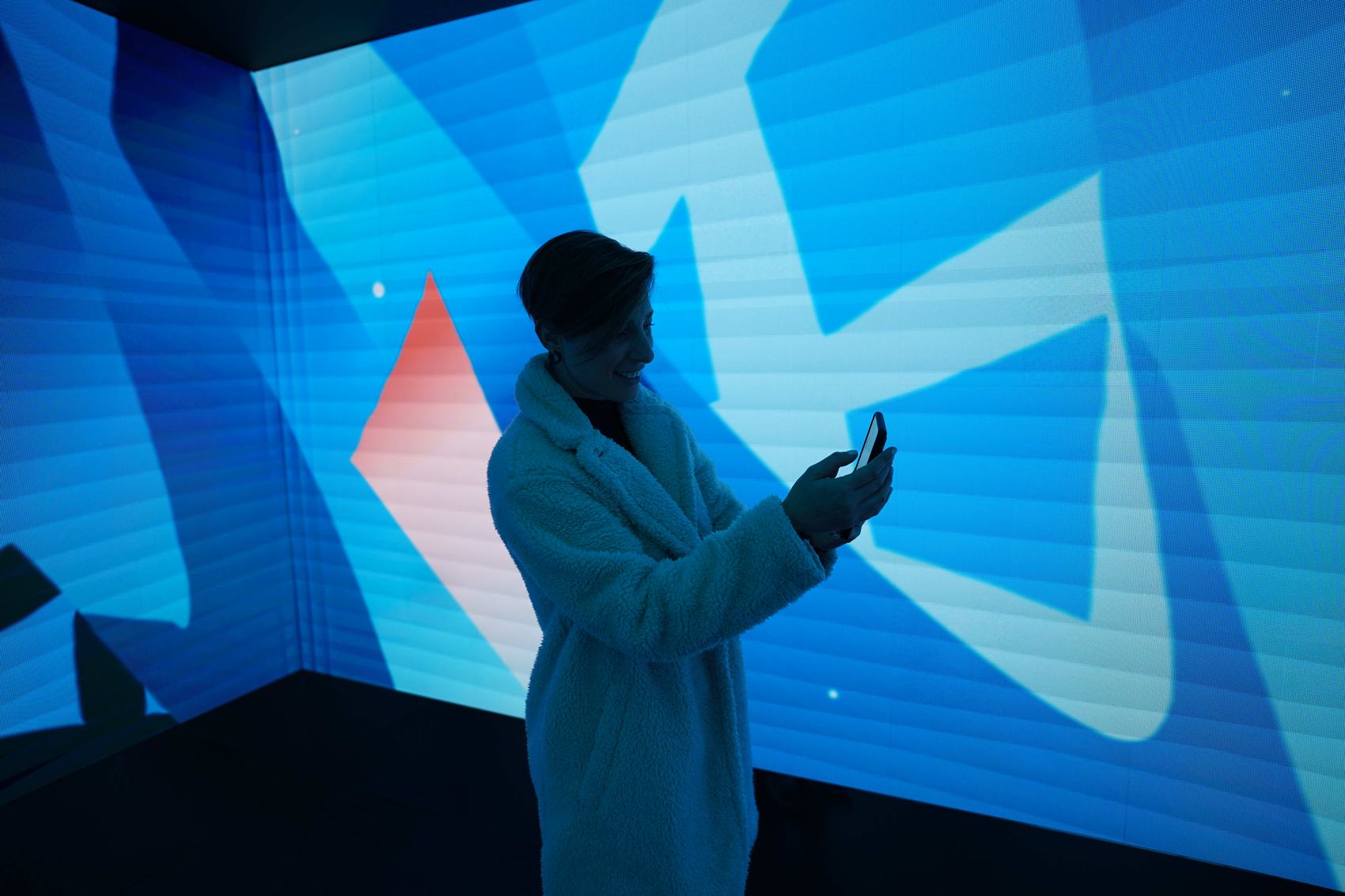 A visitor holding her phone to a large blue projected wall